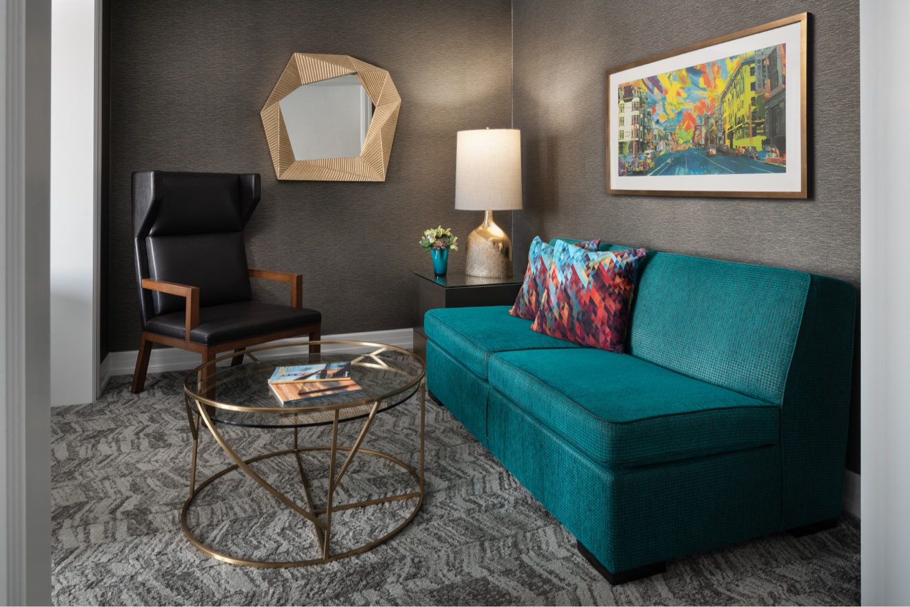 Guest suite lounge with teal sofa, brass tables, and abstract art