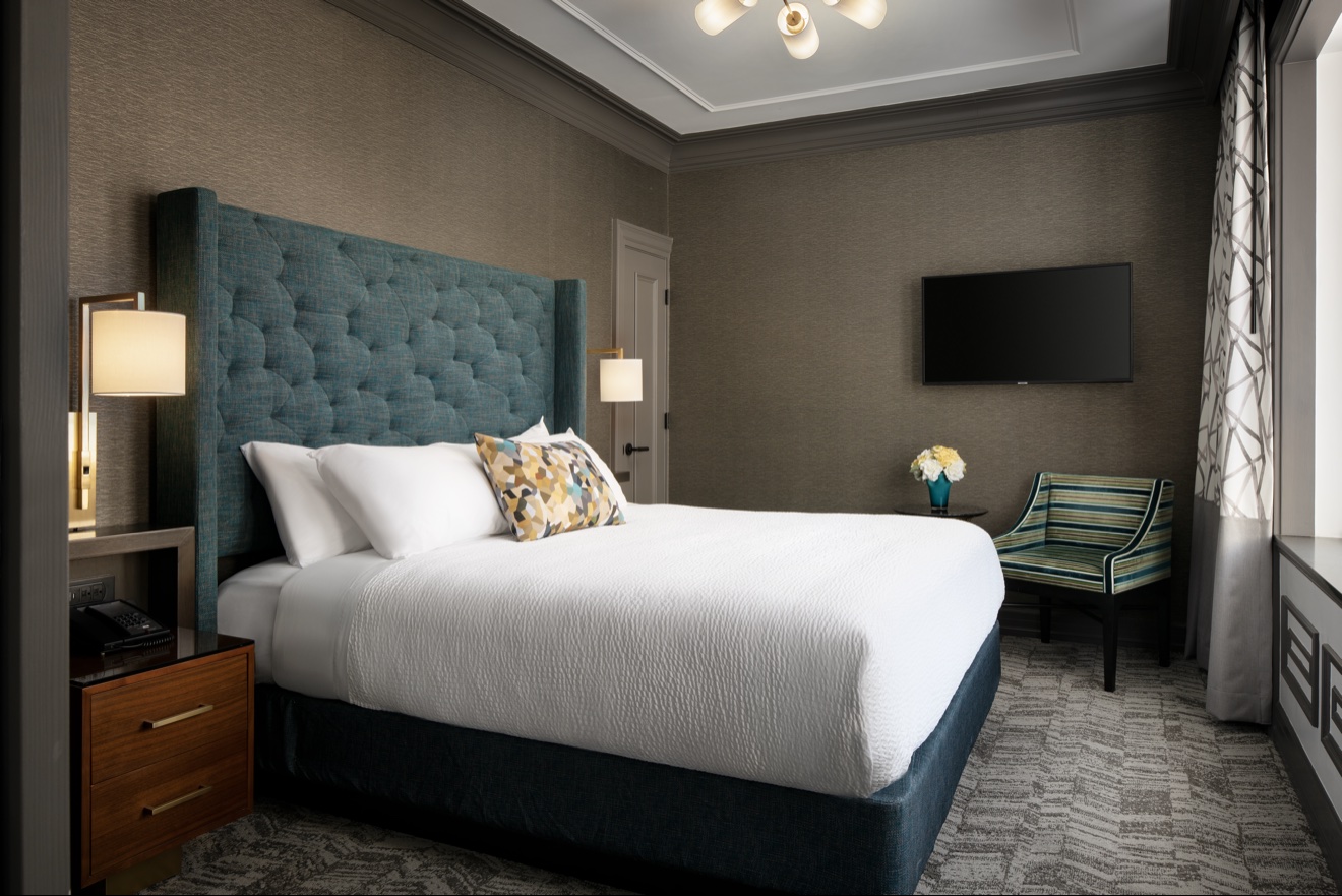 Guest room with teal upholstered bed and dark tailored furnishings