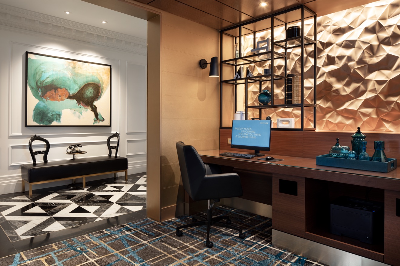 Business center with built-in walnut desk, sculptural metal wall, and adjacent lounge