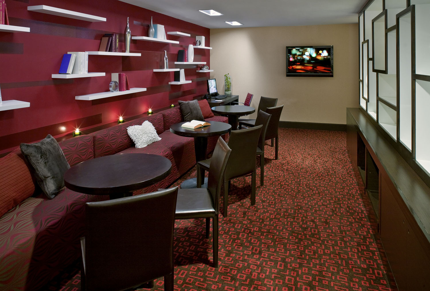 Hotel lounge with red chairs, dark tables, and a long service counter