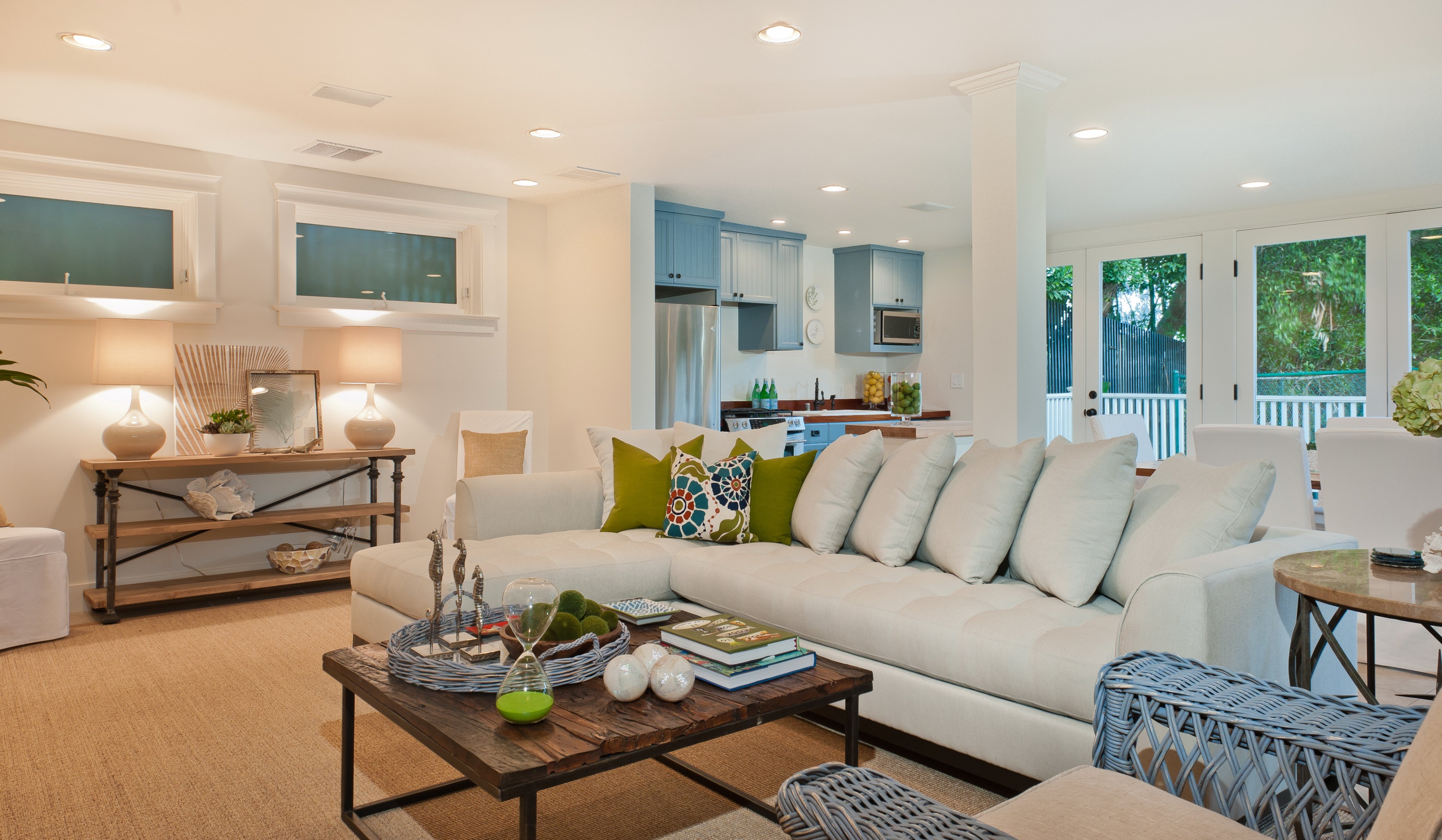 Open-plan living room and blue-cabinet kitchen opening to a leafy terrace
