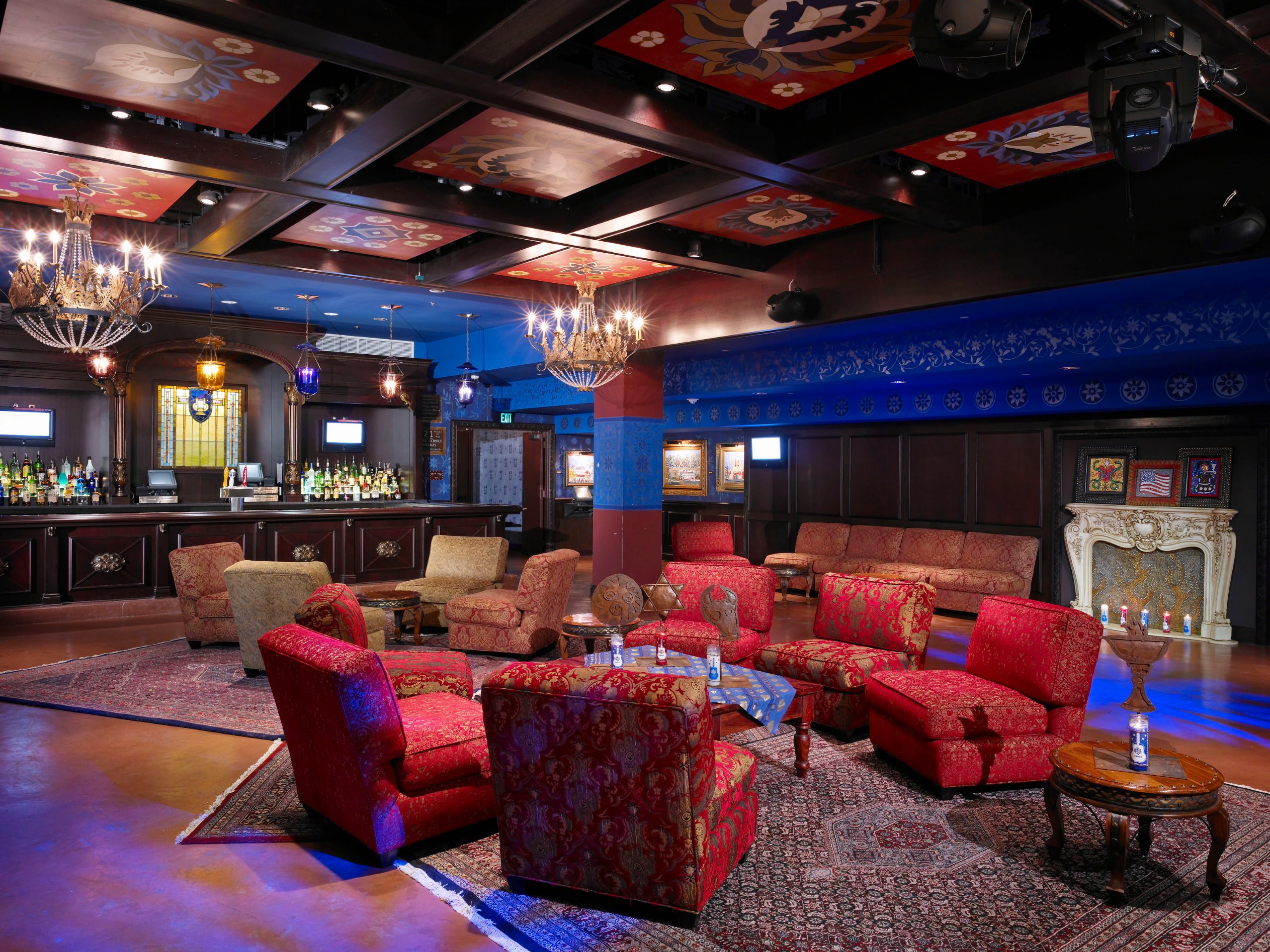 Red lounge with fireplace, chandeliers, and vivid patterned upholstery