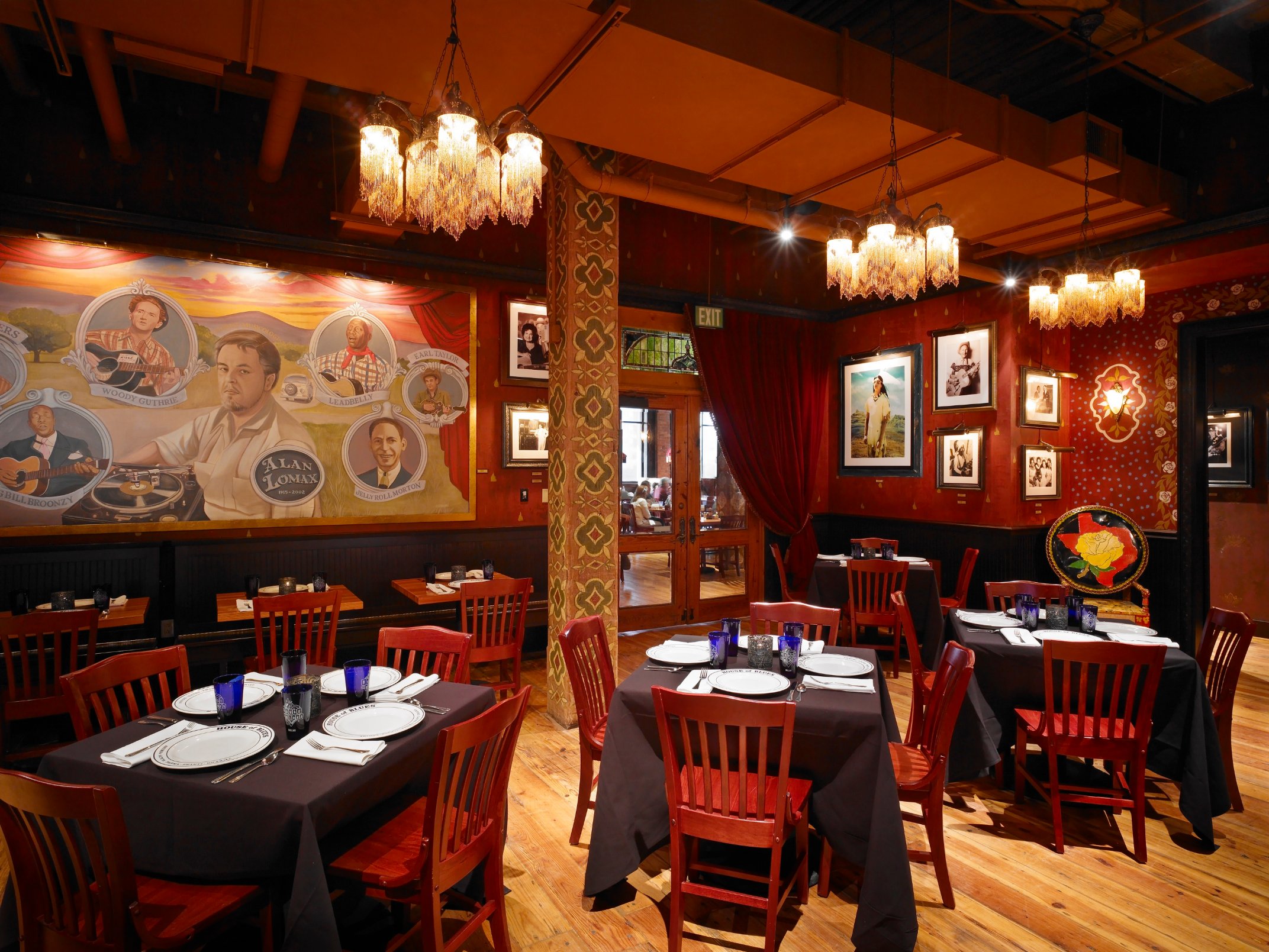 Red dining lounge with framed artwork, clustered chandeliers, and timber columns