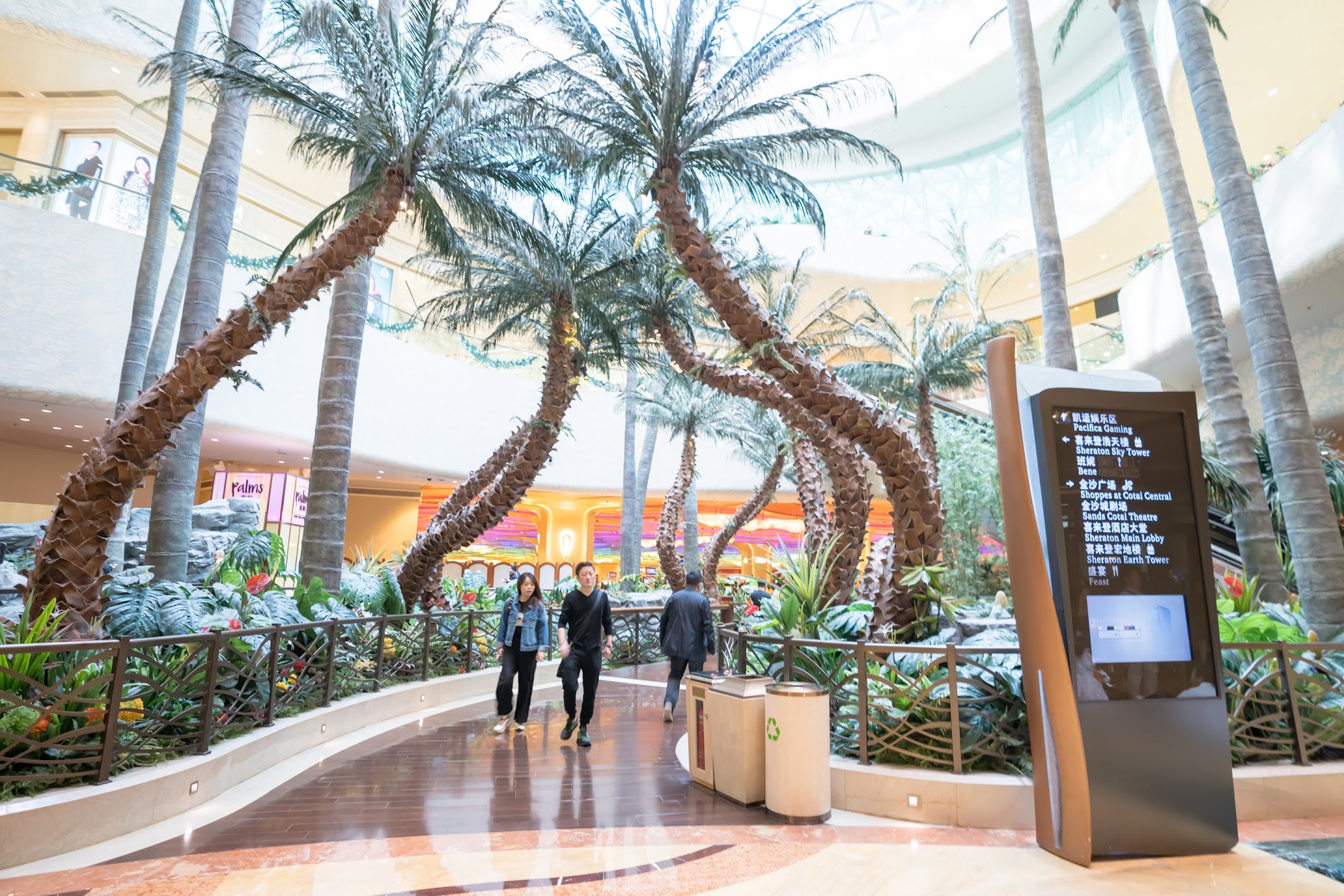 Atrium walkway lined with leaning palm trees and tropical planting