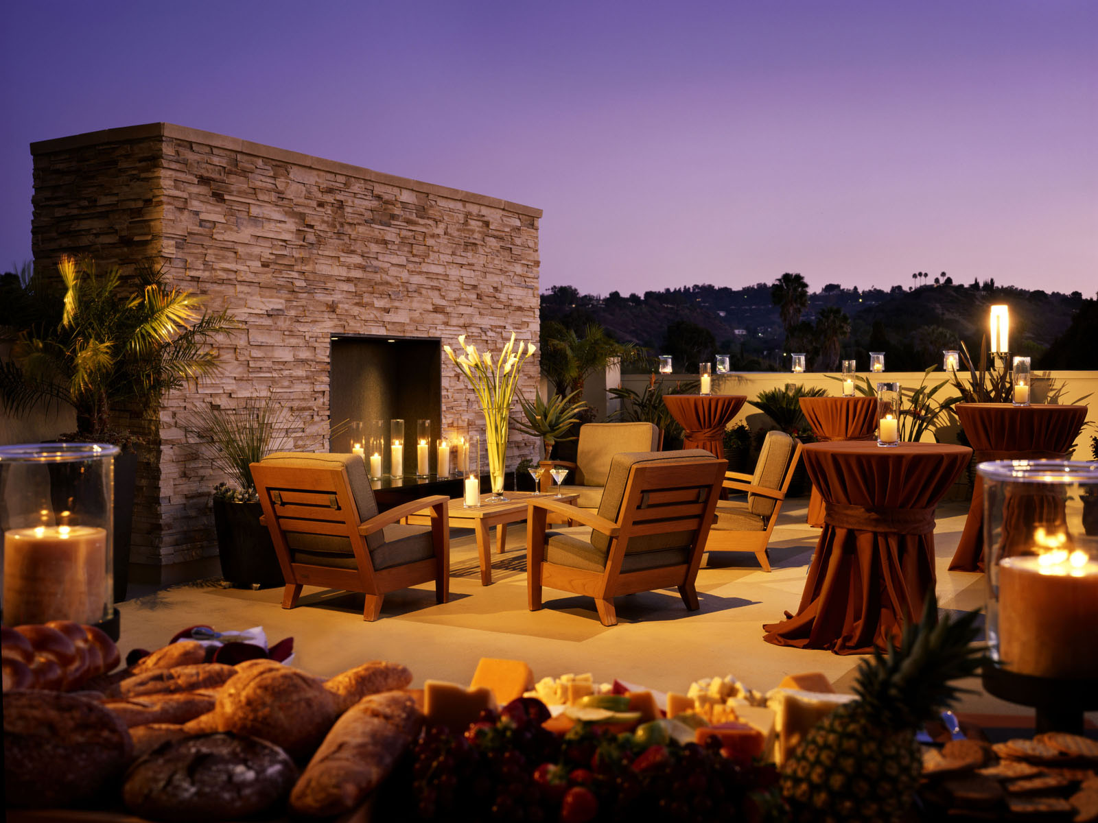 Outdoor terrace at dusk with a stacked-stone fireplace and candlelit cocktail tables