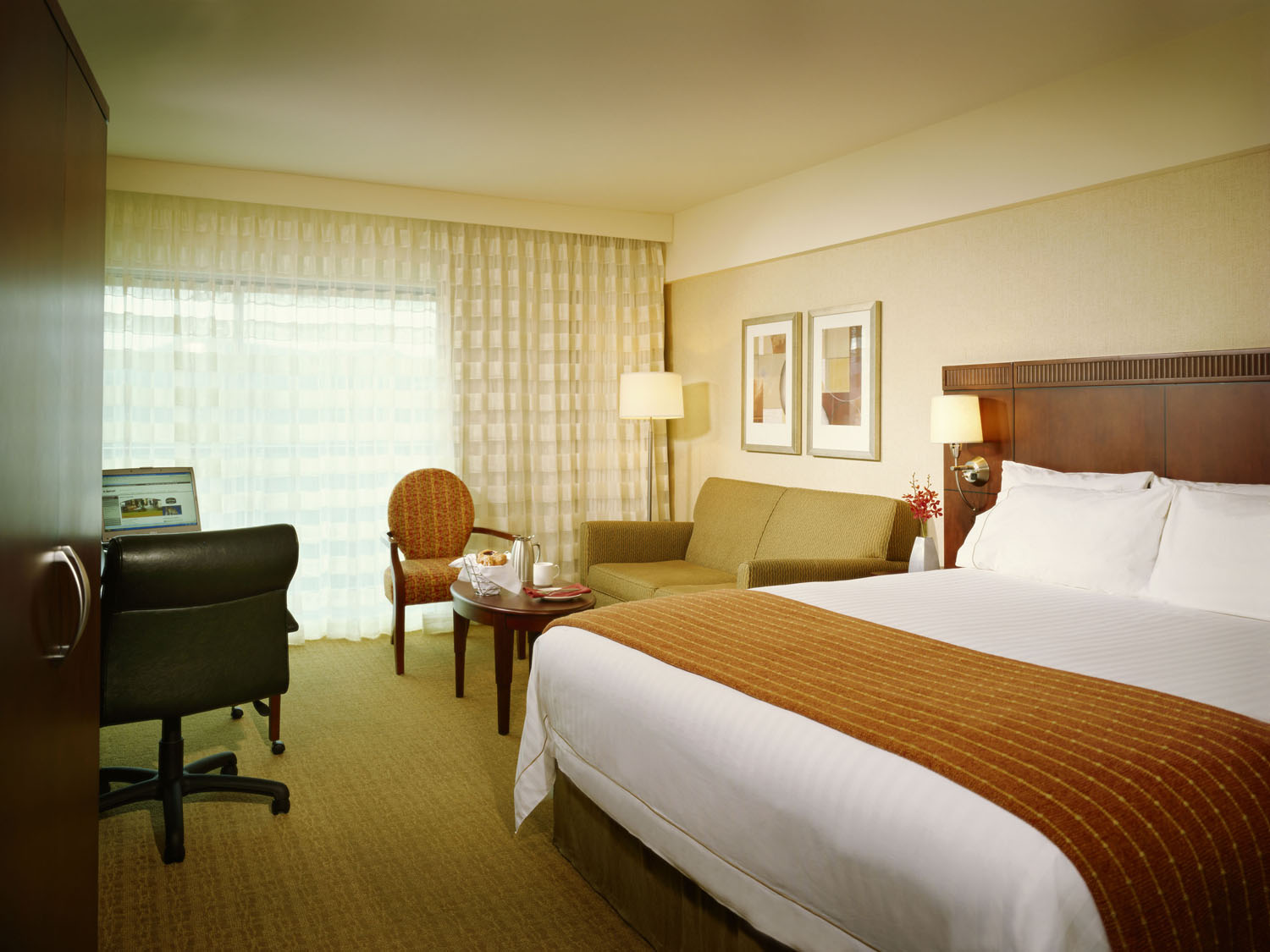 Guest room with a king bed, work desk, and sitting area beside sheer curtains