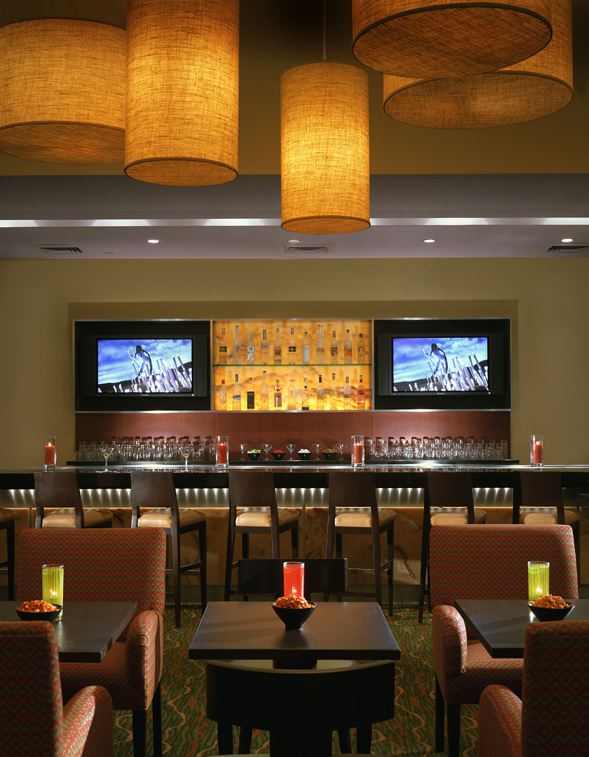 Hotel bar with woven pendant lights and a backlit bottle display